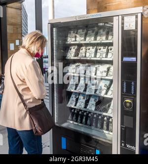 Donna che guarda un distributore automatico che vende maschere facciali a Liverpool Lime Street, Merseyside, Regno Unito. Foto Stock