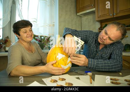 Facendo Jack o'Lantern a casa. Il processo di creazione di un modello di tema Jack o'Lantern. Un uomo e una donna stanno preparando una zucca per la scultura. Foto Stock