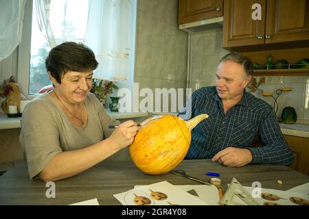 Facendo Jack o'Lantern a casa. Il processo di creazione di un modello di tema Jack o'Lantern. Un uomo e una donna stanno preparando una zucca per la scultura. Foto Stock