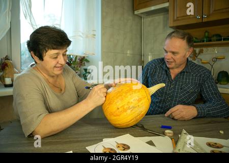 Facendo Jack o'Lantern a casa. Il processo di creazione di un modello di tema Jack o'Lantern. Un uomo e una donna stanno preparando una zucca per la scultura. Foto Stock