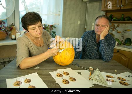 Facendo Jack o'Lantern a casa. Il processo di creazione di un modello di tema Jack o'Lantern. Un uomo e una donna stanno preparando una zucca per la scultura. Foto Stock