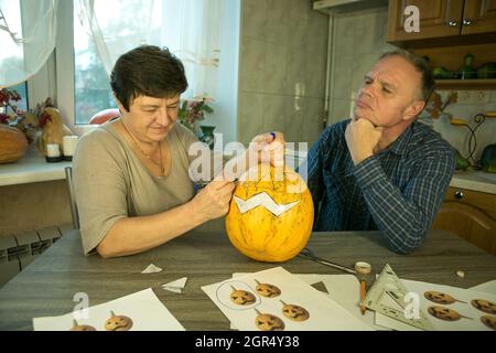 Facendo Jack o'Lantern a casa. Il processo di creazione di un modello di tema Jack o'Lantern. Un uomo e una donna stanno preparando una zucca per la scultura. Foto Stock