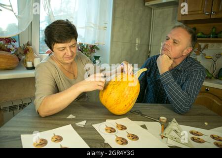 Facendo Jack o'Lantern a casa. Il processo di creazione di un modello di tema Jack o'Lantern. Un uomo e una donna stanno preparando una zucca per la scultura. Foto Stock