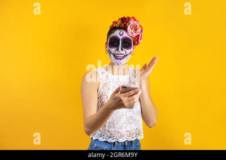 Catrina messicana, ritratto di giovane donna latina che tiene il telefono cellulare per la festa di Halloween in Messico Foto Stock