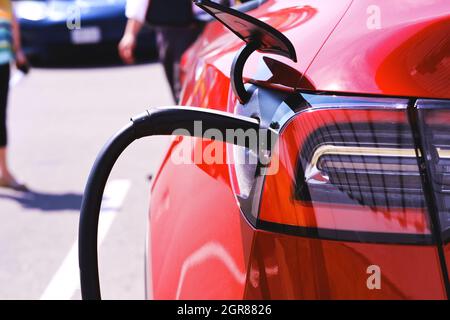 Ricarica di auto elettriche Red Tesla presso la concessionaria. Le vendite mostrano la vettura nuova al cliente nel parcheggio in background. Foto Stock