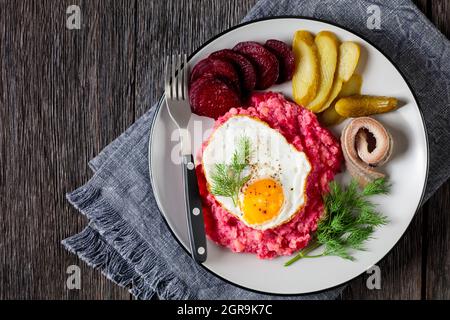 labskaus, carne di manzo, purè di patate con barbabietole ricoperte di uova fritte, barbabietole affettate, sottaceti e aringhe arrotolate su un piatto, cui tedesco Foto Stock