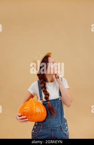 Donna giardiniere tiene una zucca grande su uno sfondo giallo. Foto Stock