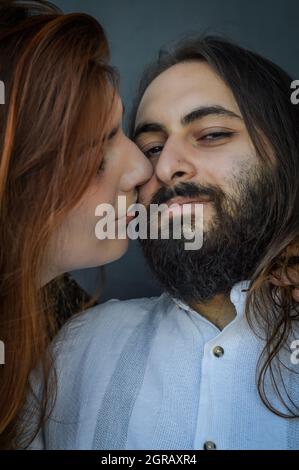 Ritratto di una giovane coppia in cui una lunga donna dai capelli rossi bacia con capelli lunghi la guancia dell'uomo dell'uomo bearded Foto Stock