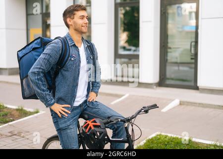 Ritratto di felice bel giovane uomo di consegna con termo zaino ragazzo seduto in bicicletta riposo dopo la consegna on-line ordine al cliente Foto Stock