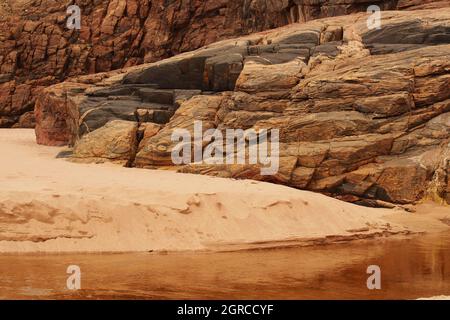 Strutture naturali di roccia e sabbia nella baia di Sandwood, Sutherland, Scozia, dove un fiume entra sulla spiaggia mostrando la roccia dei gneiss di Lewisian Foto Stock