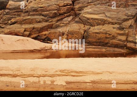 Strutture naturali di roccia e sabbia nella baia di Sandwood, Sutherland, Scozia, dove un fiume entra sulla spiaggia mostrando la roccia dei gneiss di Lewisian Foto Stock