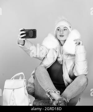 ragazza in cappotto soffiato fare selfie. faux moda pelliccia. caldo abbigliamento invernale. telefono selfie. influenza e stagione fredda. Borsa in pelle moda. Donna in berretto Foto Stock