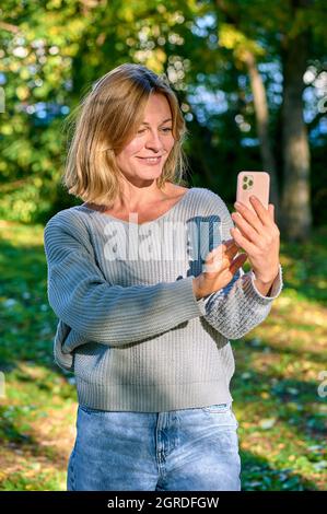 Una donna in un parco in estate parla durante una videochiamata al telefono Foto Stock