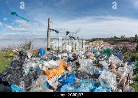 Sacchetti di plastica soffiati da una discarica a Grahamstown/Makhana, Sudafrica, catturati in una recinzione. Il fumo di un incendio della discarica riempie l'aria. Foto Stock