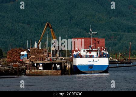 La barca ormeggiata a Dunoon è stata caricata con legname dalla Foresta Argyll raffigurata sullo sfondo. Foto Stock