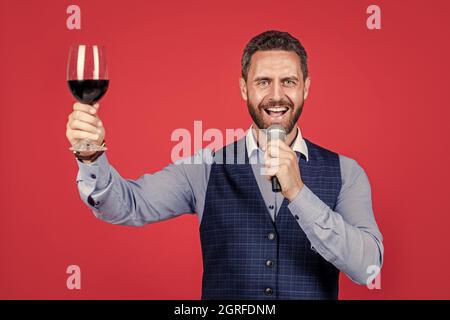 Chiedo che il banchetto continui. Toastmaster parla nel microfono alzando un bicchiere di vino. Banchetto in attesa. Cerimonia o celebrazione. Di pubblico dominio Foto Stock