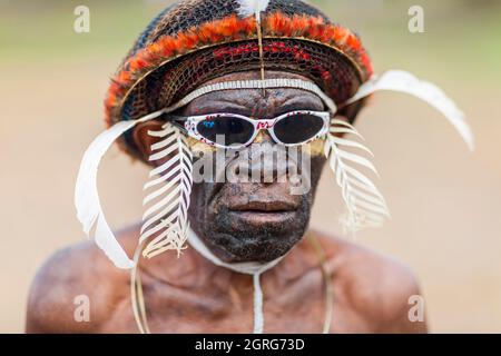 Indonesia, Papua, città di Wamena, ritratto di un uomo della tribù Dani, con occhiali da sole. Baliem Valley Cultural Festival, ogni agosto, le tribù si riuniscono per eseguire scene di guerra ancestrali, sfilate e danze in abiti tradizionali Foto Stock