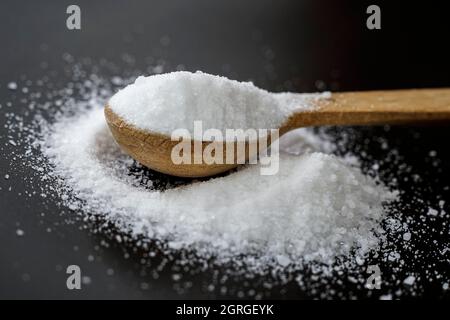 Cucchiaio da tè in legno pieno di sale marino isolato su sfondo nero Foto Stock