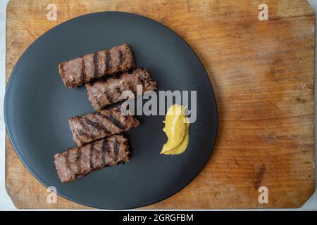 Carne tritata alla griglia tradizionale rumena, mici o mititei su un piatto di ceramica nera con senape Foto Stock