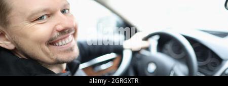 Il giovane sorridente si siede nel salone dell'automobile dietro la ruota Foto Stock