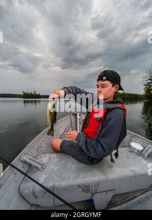 Ragazzino che tiene un pesce catturato in una barca in una giornata di tempesta. Foto Stock