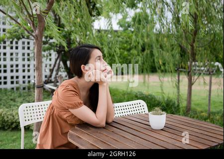 Solitudine giovane donna asiatica seduta e mettere le mani prop su mento e guardare qualcosa in giardino Foto Stock