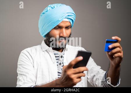 Giovane uomo sikh che acquista pagando in linea usando la carta di credito nel telefono mobile - concetto di shopping in linea o di ordine dal e-commercio. Foto Stock