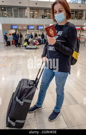 Giovane donna con maschera facciale, passaporto e valigia all'aeroporto internazionale o alla stazione ferroviaria. Concetto di viaggio nel tempo del covid 19 pandemi Foto Stock