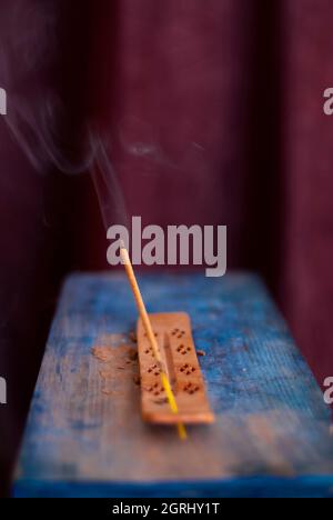 bastone di incenso illuminato con filo di fumo con sfondo scuro su base blu cielo Foto Stock