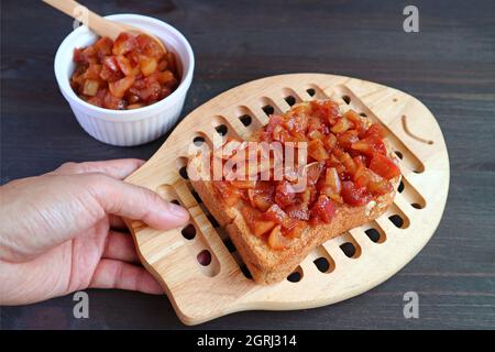 Mano dell'uomo che tiene il breadboard del toast fatto in casa della composta di mele che mette sul tavolo nero Foto Stock