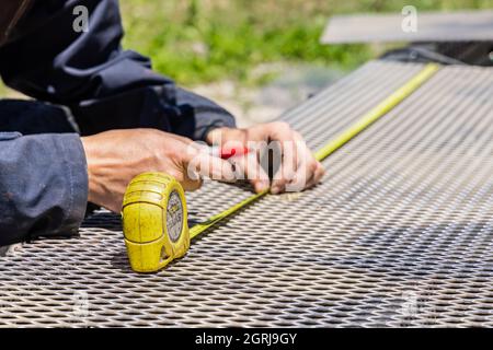 Un colpo di mani di saldatore che tiene una penna e un nastro di misurazione giallo, che effettua misurazioni di una superficie metallica con precisione e abilità. Foto Stock