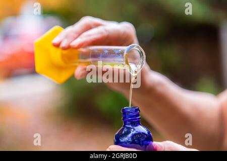 : Uno zoomato in vista delle mani, portando la bottiglia blu, versando liquido dal vetro trasparente, il liquido è un olio essenziale utilizzato per l'aromaterapia. Foto Stock