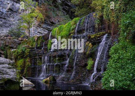 muro di pietra nera con cascate che cadono tra la foresta e la vegetazione, rupit catalogna, spagna Foto Stock