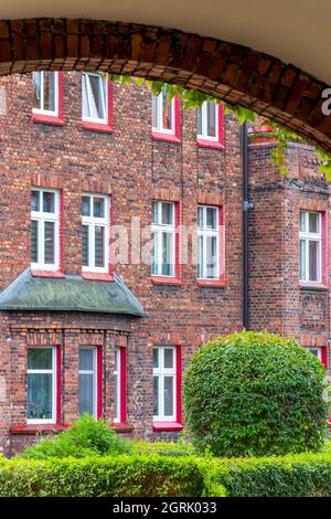 Cortile nel tradizionale quartiere silesiano Nikiszowiec a Katowice, in Polonia, visto attraverso il portone arcade. Vecchie case in mattoni con finestra dipinta di rosso fra Foto Stock