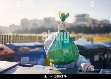 Uomo che cammina con rifiuti. Portare a mano il sacchetto di plastica contro i bidoni della spazzatura sulla strada. Foto Stock