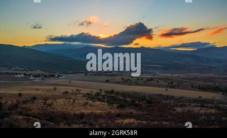 Tramonto colorato sulle montagne. Ampio panorama che si affaccia sul paese e campi agricoli Foto Stock