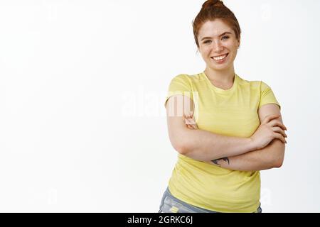 Sorridente giovane donna curvo che fa gli esercizi sportivi, le braccia incrociate sul petto, l'allenamento per essere sano, in piedi su sfondo bianco Foto Stock