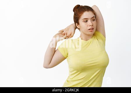 Ritratto di rosso più taglia donna stretching braccio dietro la schiena, esercizi di fitness warm-up in palestra, in piedi su sfondo bianco Foto Stock