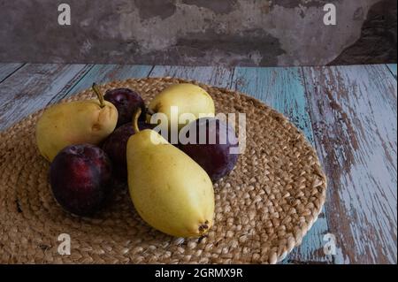 Le pere e le prugne si trovano su tovaglioli di vimini sulle tavole in stile provenzale contro il muro di mattoni rossi Foto Stock