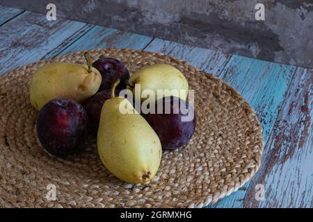 Le pere e le prugne si trovano su tovaglioli di vimini sulle tavole in stile provenzale contro il muro di mattoni rossi Foto Stock