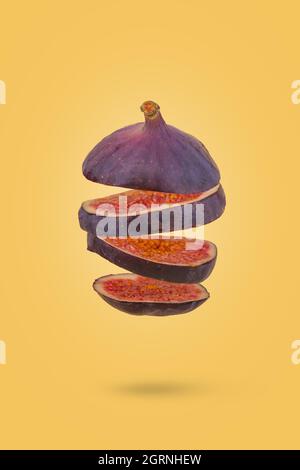 Fico fresco affettato tagliato a fette volare in aria isolato su sfondo giallo pastello. Concetto di cibo creativo. Idea di dieta vegetariana. Foto Stock