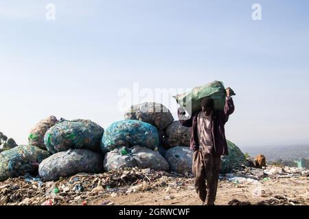 Nakuru, Kenya. 01 ottobre 2021. Un uomo porta un sacco di rifiuti riciclabili sulle spalle a un impianto di riciclaggio vicino al sito di scarico di Gioto a Nakuru.il problema crescente dei rifiuti di plastica che finiscono nell'ambiente sta diventando una preoccupazione e gli ambientalisti stanno chiedendo maggiori investimenti nelle infrastrutture per riciclare la plastica per promuovere economia circolare e ridurre l'inquinamento della plastica. Essi chiedono inoltre al governo di introdurre un sistema obbligatorio di deposito e rimborso delle bottiglie (DRS) che darà valore alle bottiglie di plastica per bevande comunemente note come animali da compagnia (polietilentereftalato). Deposito refu Foto Stock