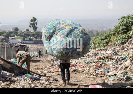 Nakuru, Kenya. 01 ottobre 2021. Un uomo porta un carico pesante di rifiuti di bottiglie di plastica sulle sue spalle a un impianto di riciclaggio vicino al sito di scarico di Gioto a Nakuru. Il problema crescente dei rifiuti di plastica che finiscono nell'ambiente sta diventando una preoccupazione e gli ambientalisti stanno chiedendo maggiori investimenti nelle infrastrutture per riciclare la plastica promuovere l'economia circolare e ridurre l'inquinamento della plastica. Essi chiedono inoltre al governo di introdurre un sistema obbligatorio di deposito e rimborso delle bottiglie (DRS) che darà valore alle bottiglie di plastica per bevande comunemente note come animali da compagnia (polietilentereftalato). De Foto Stock