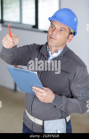 uomo ingegnere che indossa il casco tenendo gli appunti puntati Foto Stock