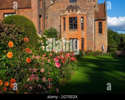 Chenies Manor House in Autumn.Plant confine con grandi fiori di dahlia arancione e rosa portare l'occhio alle finestre della baia del maniero Tudor nel mese di settembre. Foto Stock