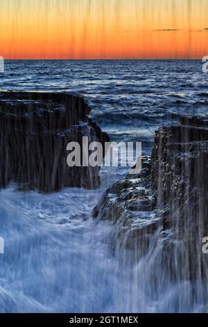 Gocce e corde di spruzzi d'onda in arrivo sulle rocce della spiaggia di Narrabeen sulla costa pacifica delle spiagge del Nord di Sydney all'alba. Foto Stock