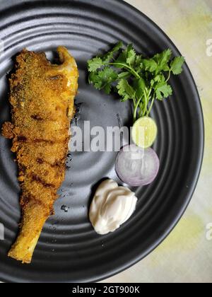 Frittura di pesce intero servita sul piatto. Preparazione in stile malabar indiano decorata con coriandolo, cipolla. Pasto perfetto ad alto contenuto proteico. Primo piano. Foto Stock