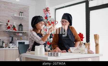 I nipoti indossano il grembiule mentre preparano il delizioso pan di zenzero fatto in casa utilizzando i biscotti di Natale a forma di cucina culinaria. Famiglia felice godersi natale vacanza di cucina tradizionale dessert Foto Stock