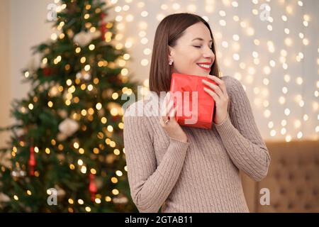 Ritratto di giovane donna felice labbra rosse in posa con una confezione regalo avvolta. Primo piano la donna soddisfatta ha ricevuto la scatola presente. Natale festivo luci sfondo. Foto Stock