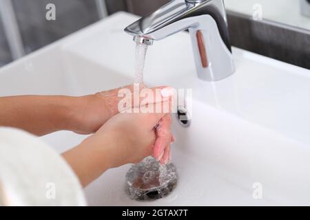 La donna lava le mani sotto l'acqua corrente nel lavabo in primo piano Foto Stock